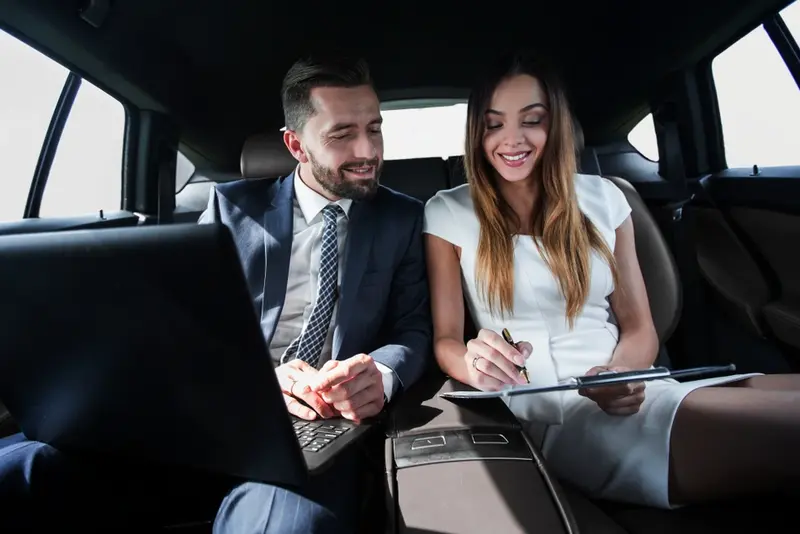 Business professionals using a luxury black car service for a mobile office, working on a laptop and documents during transit.